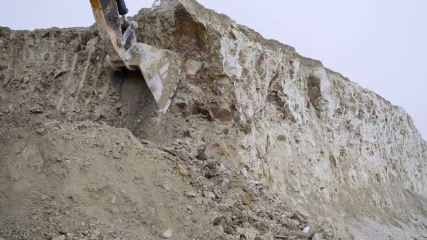 A large excavator bucket digs a quarry with hard rock. A mighty bulldozer unleashes its power on a huge pile of earth.
