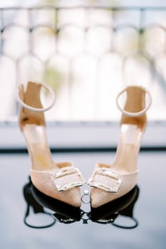 Engagement ring stands between the toes of the bride golden high-heeled shoes on the mirror floor. High quality photo