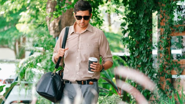 Young handsome man walk out of coffee shop with cafe garden, holding a coffee cup and a shopping bag. Modern happy carefree with sunglasses lifestyle. Expedient