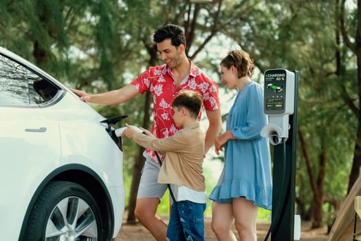 Outdoor adventure and family vacation camping in nature travel by eco friendly car for sustainable future. Lovely family recharge EV car with EV charging station in campsite. Perpetual