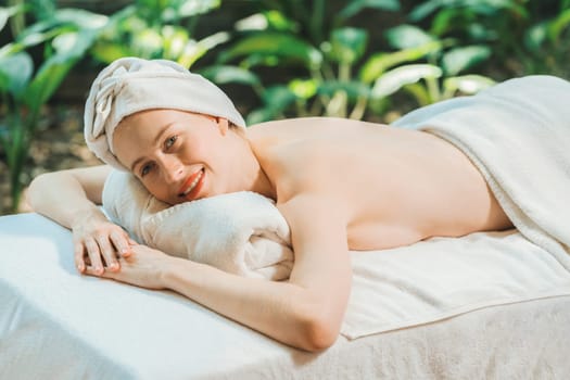 A beautiful young woman lies on a spa bed while looking at camera. Feeling of relaxed and at peace. Attractive caucasian woman surrounded by the calming sounds of nature. Tranquility