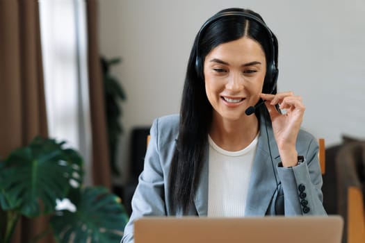 Female call center operator or customer service helpdesk staff working on workspace while talking on the headset to provide assistance for customer. Professional modern business service. Blithe