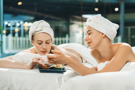 Couple of beautiful young girls lie on spa bed during interested in homemade beauty facial mask. Attractive woman touching herbal facial mask. Surrounded with nature environment. Tranquility.