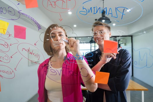 Couple of young creative start up business people brainstorming idea and solving problems by using sticky note and mind map at glass board, meeting room. discussing, working together. Immaculate.