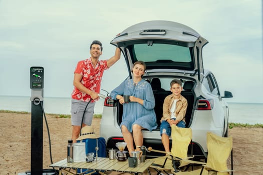 Family vacation trip traveling by the beach with electric car, happy family recharge EV car, enjoying outdoor camping coffee. Seascape travel and eco-friendly car for clean environment. Perpetual