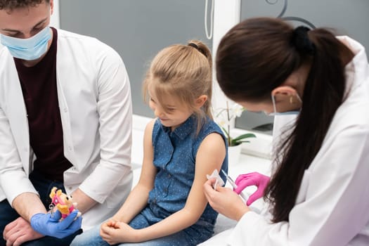 An apprentice from a medical university with a good approach to young children encourages a girl who came to a doctor's office for a vaccination for the first time in her life. Safe vaccination of children.