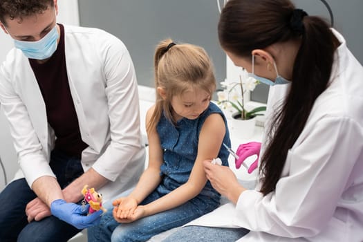 An apprentice from a medical university with a good approach to young children encourages a girl who came to a doctor's office for a vaccination for the first time in her life. Safe vaccination of children.