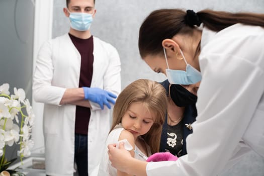 The girl came to the vaccination with her grandmother to feel safe in the doctor's office. A young nurse is injecting a new vaccine. Safe vaccination of children.