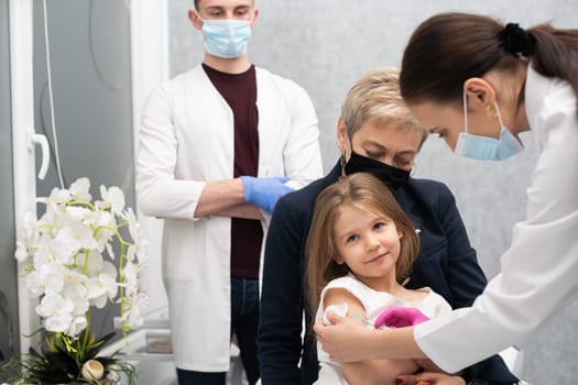 The girl came to the vaccination with her grandmother to feel safe in the doctor's office. A young nurse is injecting a new vaccine. Safe vaccination of children.