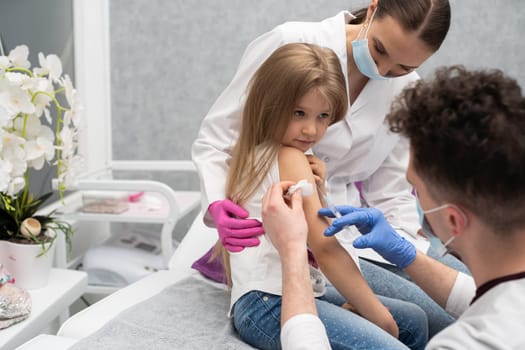 The nurse is sitting next to the girl about to be vaccinated by the doctor. A doctor's office in a public hospital. Safe vaccination of children.