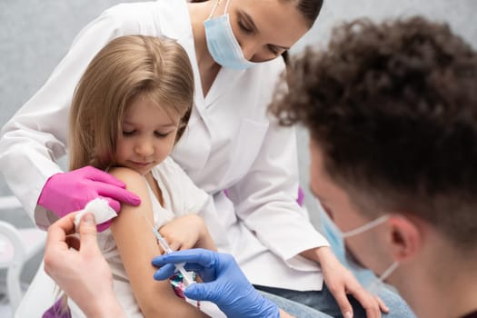 The nurse is sitting next to the girl about to be vaccinated by the doctor. A doctor's office in a public hospital. Safe vaccination of children.