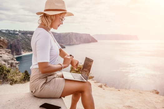 Digital nomad, Business woman working on laptop by the sea. Pretty lady typing on computer by the sea at sunset, makes a business transaction online from a distance. Freelance remote work on vacation