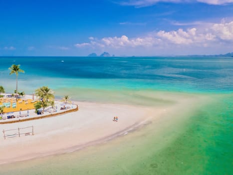 a couple of men and woman walking at the beach during a tropical vacation in Thailand, Koh Muk a tropical island with palm trees soft white sand, and a turqouse colored ocean in Thailand