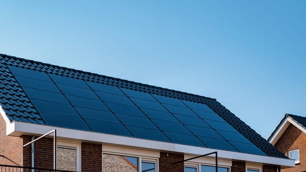 Newly built houses with black solar panels on the roof against a sunny sky Close up of new building with black solar panels in the Netherlands. Zonnepanelen, Zonne energie, Translation: Solar panel, Sun Energy