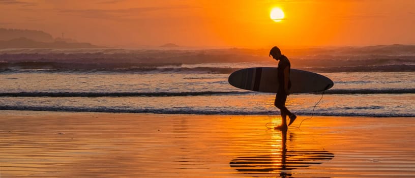 male surfer with surfboard during sunset at the beach of Tofino Vancouver Island Canada, man surfer silhouette banner with copy space