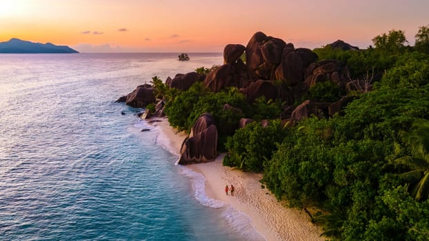 Drone top aerial view of La Digue Seychelles, a couple of men and woman walking at the beach during sunset at a luxury vacation. Anse Source d'Argent beach La Digue Island Seychelles