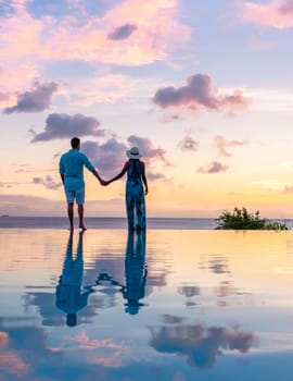 men and women watching the sunset with reflection in the infinity swimming pool at Saint Lucia Caribbean, couple at infinity pool during sunset on a tropical island during summer holiday vacation