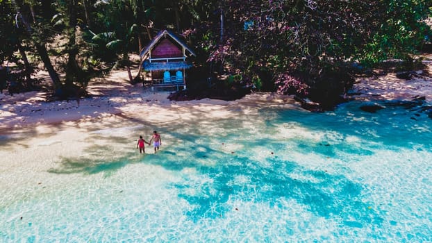 top view at a couple on a tropical beach with palm trees and a wooden bamboo hut bungalow. Koh Wai Island Trat Thailand. drone view at young man and woman on the beach