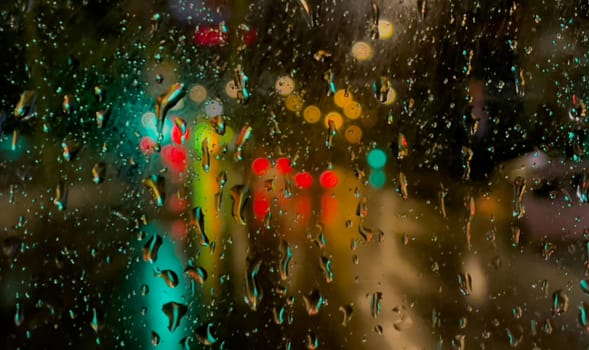 Rain bokeh road lights. Abstract shot of evening city traffic bokeh. Multicolored lights of the evening city and passing cars through a wet rainy window