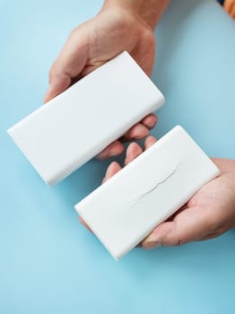 Hands comparing a new and a cracked power bank on a blue background