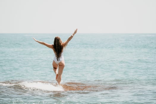 Woman sea yoga. Back view of free calm happy satisfied woman with long hair standing on top rock with yoga position against of sky by the sea. Healthy lifestyle outdoors in nature, fitness concept.