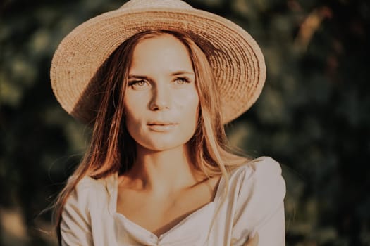 Woman with straw hat stands in front of vineyard. She is wearing a light dress and posing for a photo. Travel concept to different countries.