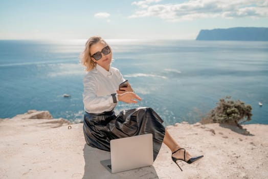 Freelance women sea working on a computer. Pretty middle aged woman with computer and phone outdoors with beautiful sea view. The concept of remote work