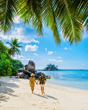 man and woman on vacation in Seychelles Mahe, a tropical beach with palm trees and a blue ocean Anse Royale Beach, a diverse couple of Asian women and caucasian men walking hand together on the beach