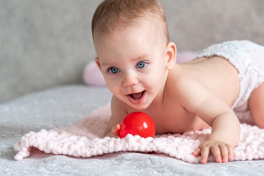 Cheerful baby playing with a red ball on a blanket.