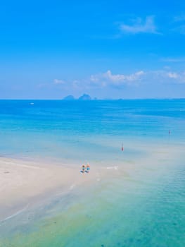 a couple of men and woman walking at the beach during a tropical vacation in Thailand, Koh Muk a tropical sandbar in a blue ocean with soft white sand, and a turqouse colored ocean Koh Mook Thailand