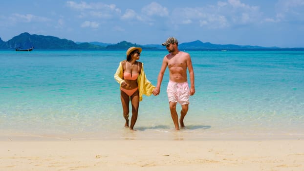 a diverse couple of men and women walking from the ocean to the beach of Koh Kradan Island Thailand, caucasian men, and Asian women summer vacation, traveling around Thailand