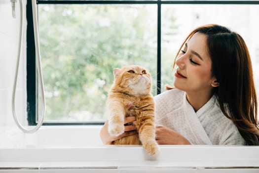 Bath time bonding, a woman holds her Scottish Fold cat in the bathtub, radiating happiness and the warmth of pet companionship in the bathroom.