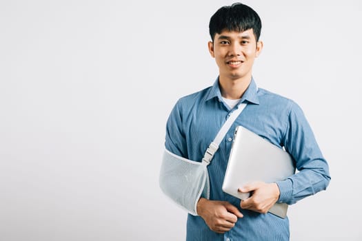 A resilient business professional, with a broken arm, utilizes a splint while working on a laptop. Studio shot isolated on white, highlighting determination and recovery. Copy space available.