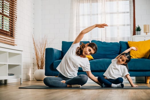 In a cozy home setting a young mother and her delightful daughter practice family yoga focusing on stretch and balance with smiles reflecting their harmonious and joyful moment.