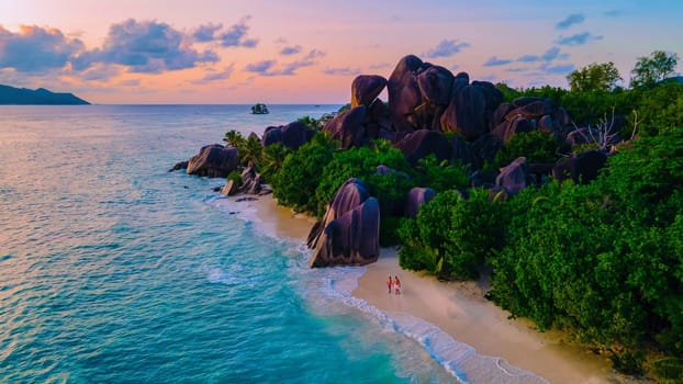 Drone top aerial view of La Digue Seychelles, a couple of men and women walking at the beach during sunset at a luxury vacation. Anse Source d'Argent beach golden hour at dusk