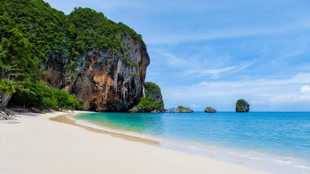 A picturesque tropical beach featuring a majestic rock formation in the background, framed by crystal clear water, blue skies, and lush green plants