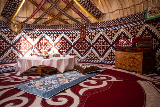 Interior of a kazak yurt with felt carpets, furniture, and a table. Traditional nomadic dwelling with white tablecloth.