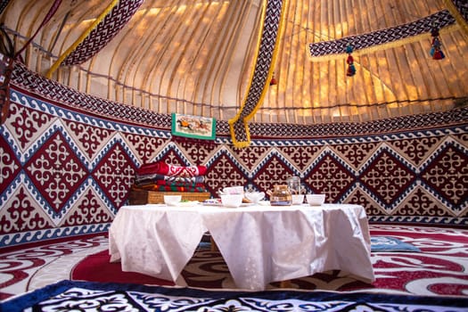 Interior of a kazak yurt with felt carpets, furniture, and a table. Traditional nomadic dwelling with white tablecloth.