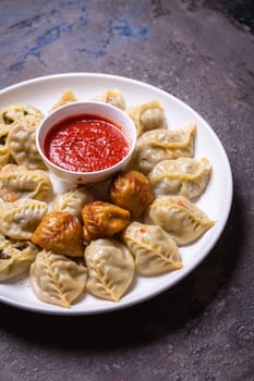 A delicious assortment of Uzbek dumplings with meat, pumpkin, and greens served on a plate with a side of red sauce