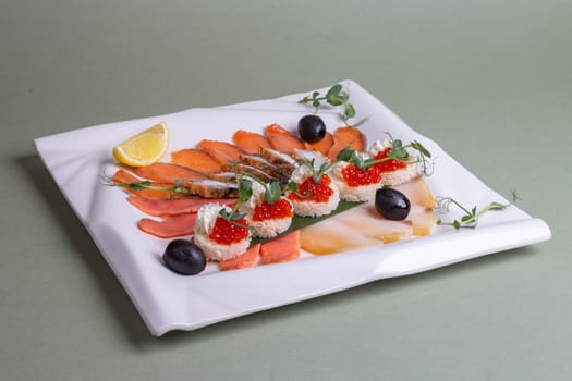 An artfully arranged platter of fresh seafood - salmon, trout, caviar, and shrimp - on a white plate with lemon slices and greens. A visually appealing still life composition.