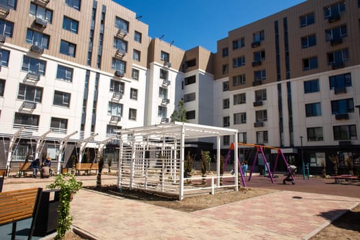 Modern apartment buildings with a courtyard playground. Contemporary design, large windows, balconies. Playground with swings, slide, climbing frame.