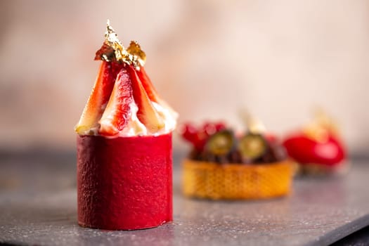 Indulgent chocolate tart, strawberry mousse, raspberry macaroon on slate board with pink background for an elegant dessert display.