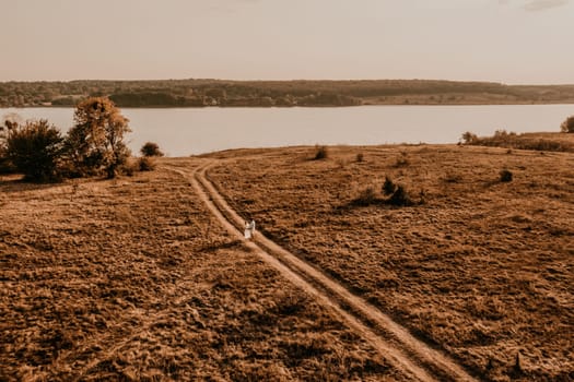 couple in love man and woman are walking along vast deserted meadow on grass in summer hot warm weather at sunset in nature. sun over river. top aerial drone view of meadows field with rare trees