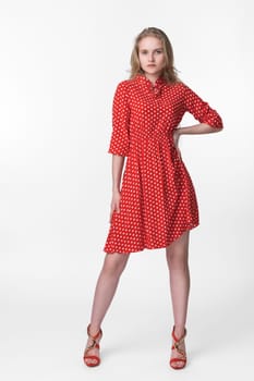 Fashionable female with long hair dressed in summer red polka dot dress, red shoes standing in full length and poses. Studio shot on white background. Caucasian woman 21 years old looking at camera