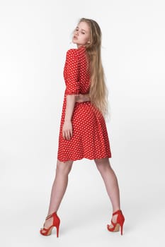 Stylish blonde woman with long hair dressed in summer red polka dot dress, red shoes standing in full length and poses. European female 21 years old looking down. Studio shot on white background