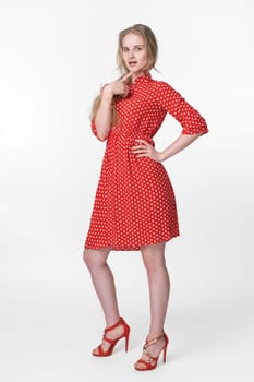 Blonde female dressed in summer red polka dot dress, red shoes standing in full length and poses on white background. Authenticity model 21 years old with long hair looking at camera. Studio shot