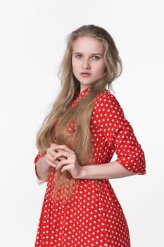 Elegant young blonde female with long hair dressed in summer red polka dot dress poses on white background. Caucasian ethnicity woman 21 years old looking at camera. Studio shot, waist up, front view