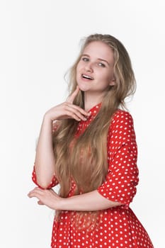 Playful young blonde female with long hair dressed in summer red polka dot dress poses on white background. Smiling Caucasian model 21 years old looking at camera. Studio shot, front view, waist up