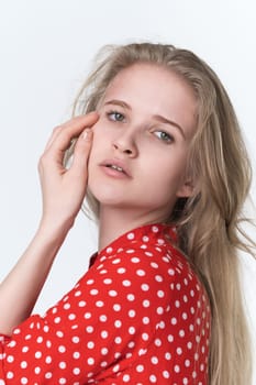 Portrait of young blonde woman with long hair looking at camera. Authenticity Caucasian female 21 years old dressed in summer red polka dot dress on white background. Studio shot, headshot