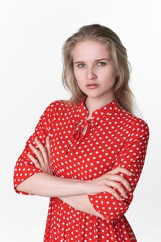 Portrait of serious young woman has her arms crossed over chest looking at camera. Ignoring Caucasian female 21 years old dressed in summer red polka dot dress. Studio headshot on white background